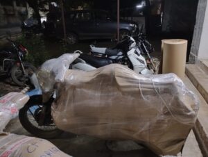 A motorcycle is fully packed in a sealed, secure crate, ready to be loaded onto a transport truck for its journey from Pune to Ahmedabad.