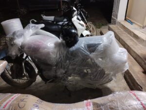 A person preparing a motorcycle in Pune for packing and transport to Ahmedabad. They are securing loose parts and draining the fuel tank.